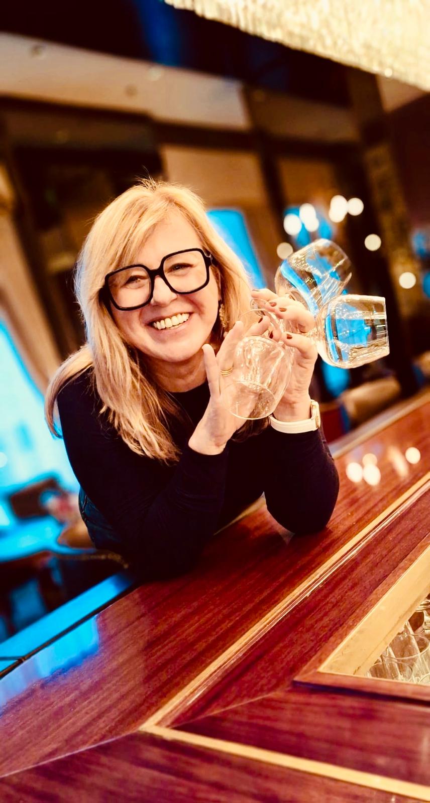 Karin Weber lächelt mit Glaswaren in einer warmen Bar-Atmosphäre